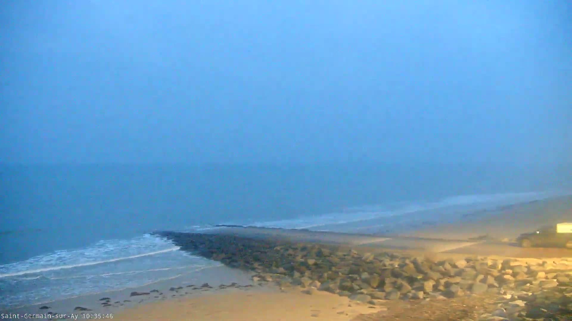 A hazy, overcast sky overlooks a rocky shoreline and a calm sea with small waves.