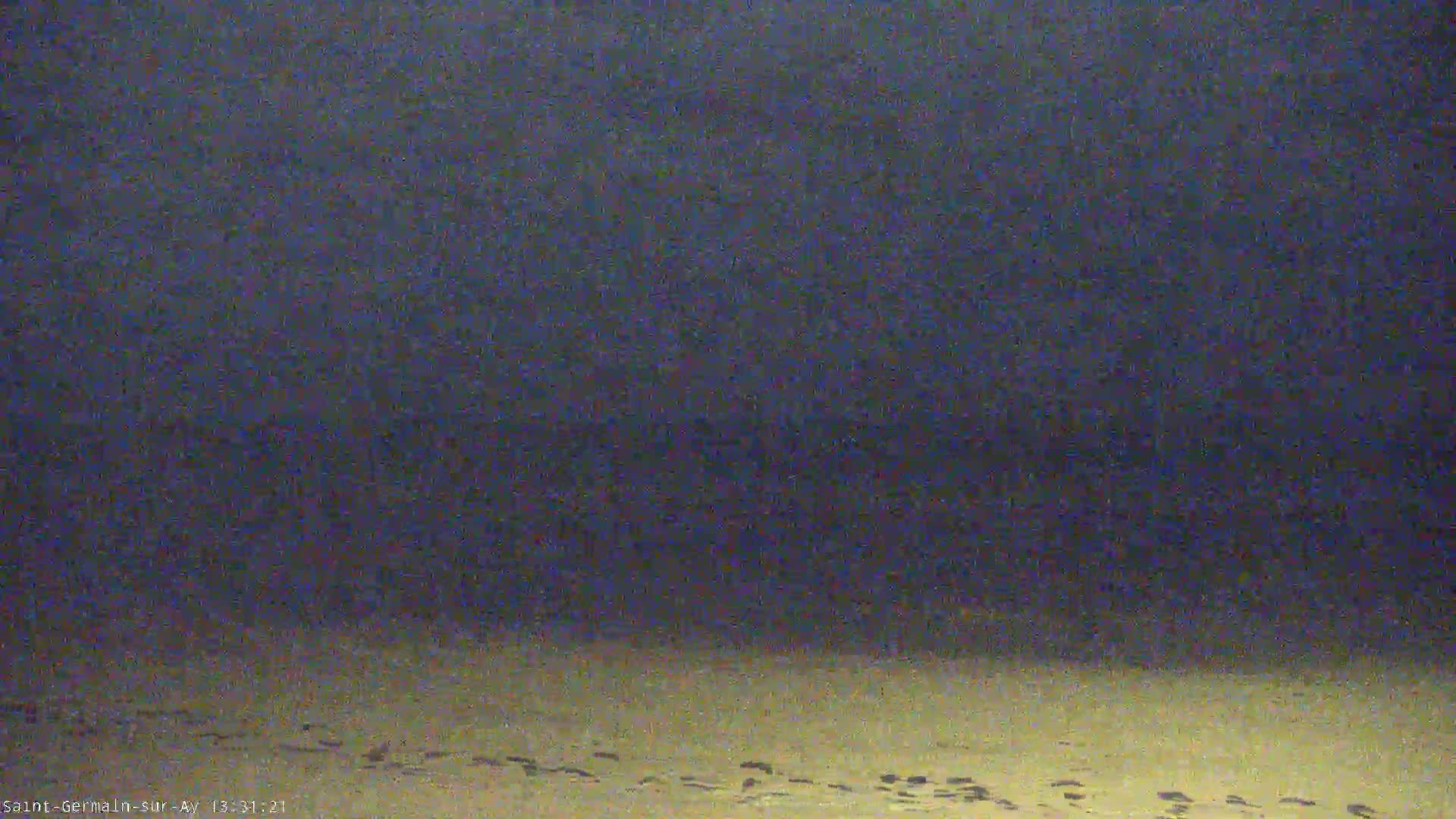 A low-light image shows a dark sky over a light-colored sandy area with numerous footprints.