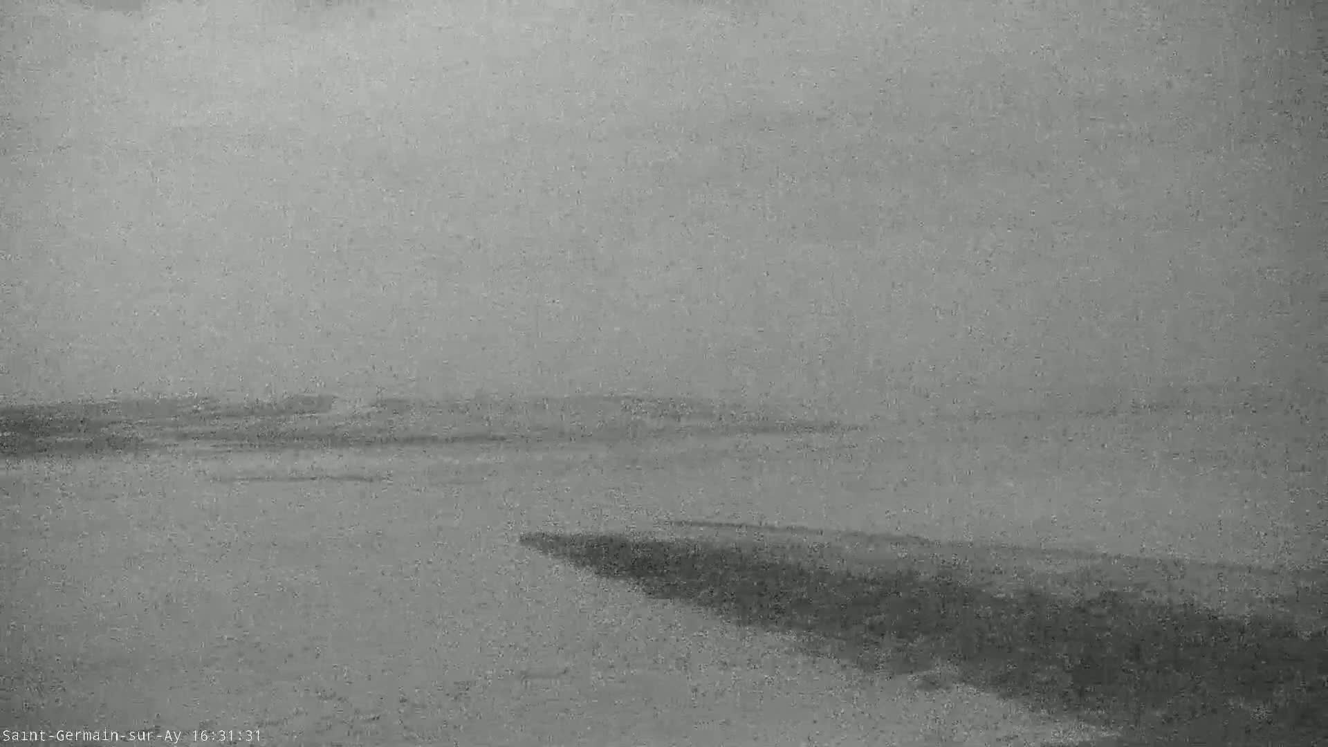 A flat, gray landscape under an overcast sky shows a body of water meeting a dark shoreline.