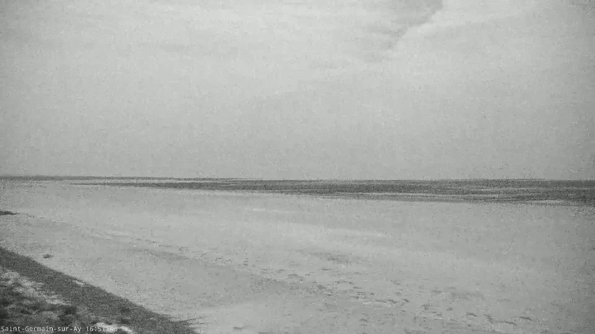 A wide shot of a flat, sandy beach meets a calm, gray ocean under an overcast sky.