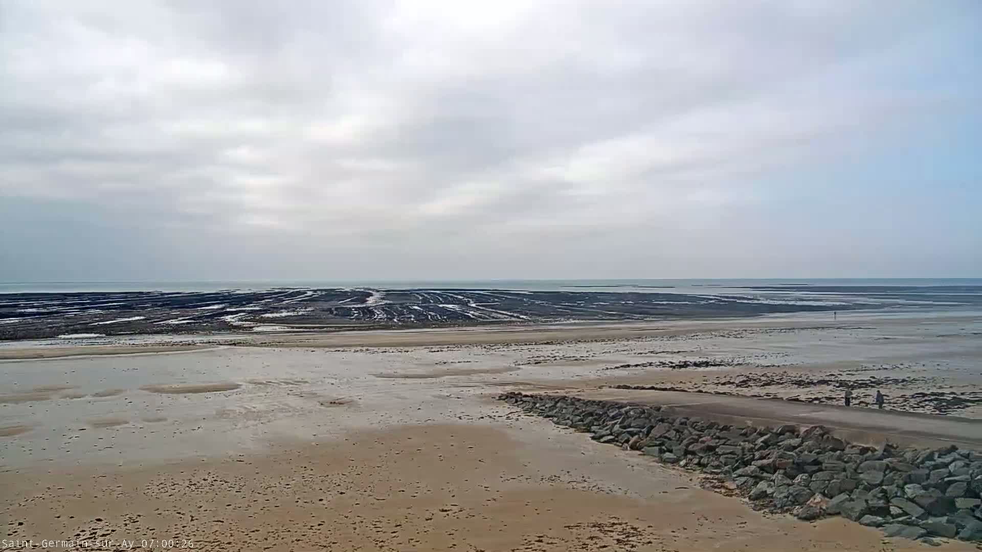 A wide sandy beach stretches to a dark, textured intertidal zone, under a cloudy sky.