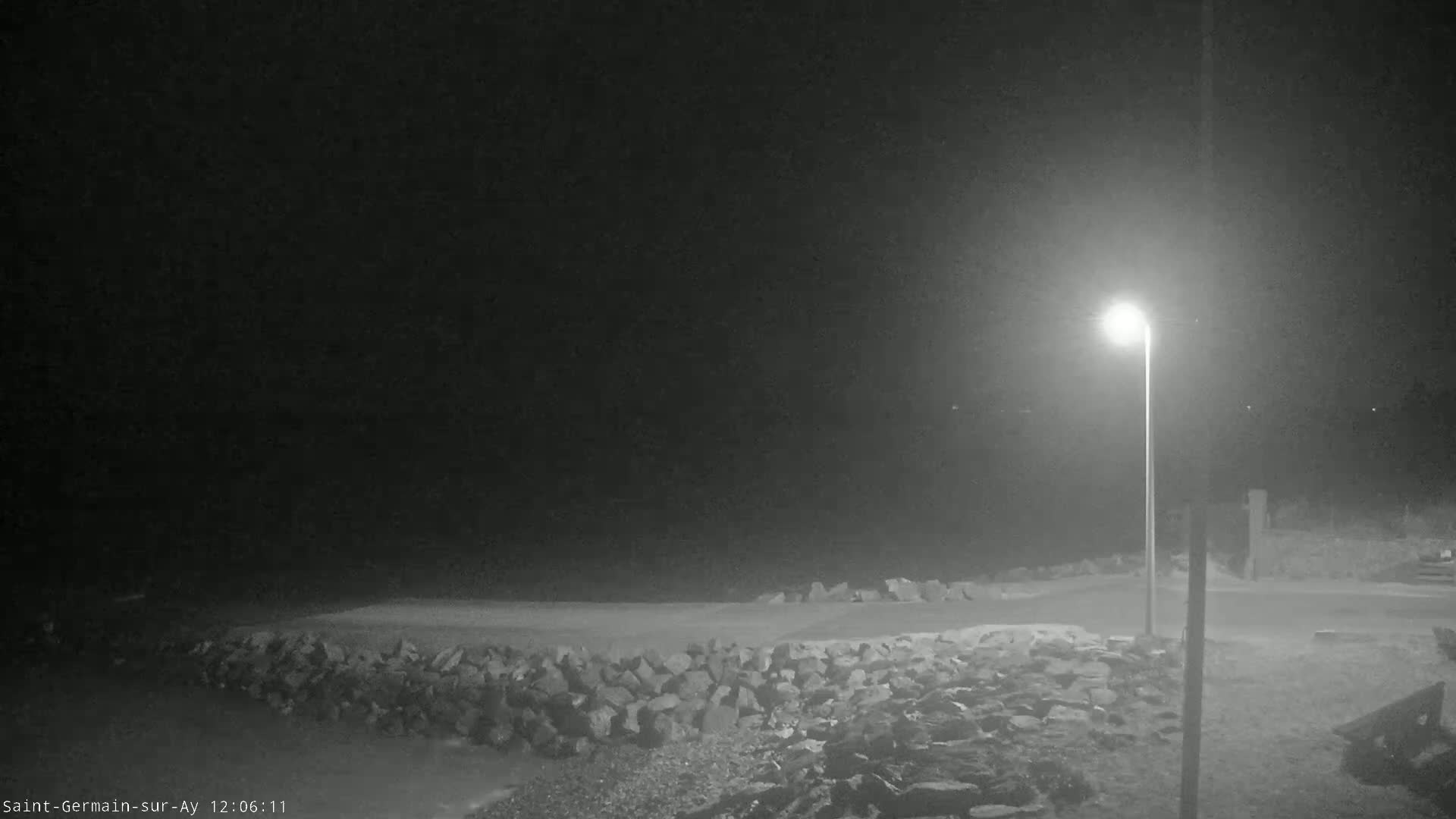 A nighttime, dimly lit outdoor scene shows a rocky shoreline and a single lamppost.
