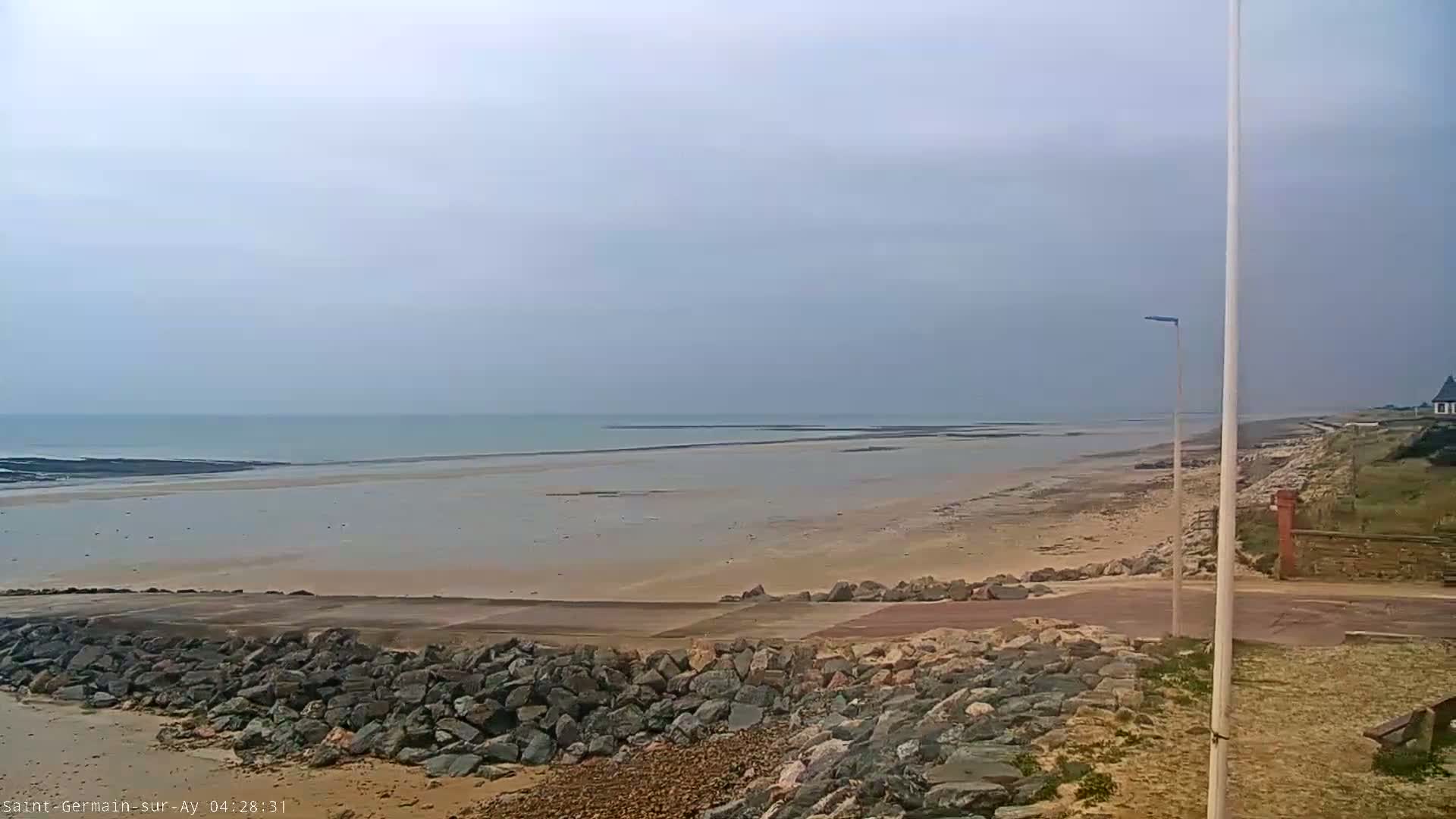 A wide, sandy beach stretches to a calm, light-blue ocean under an overcast sky.