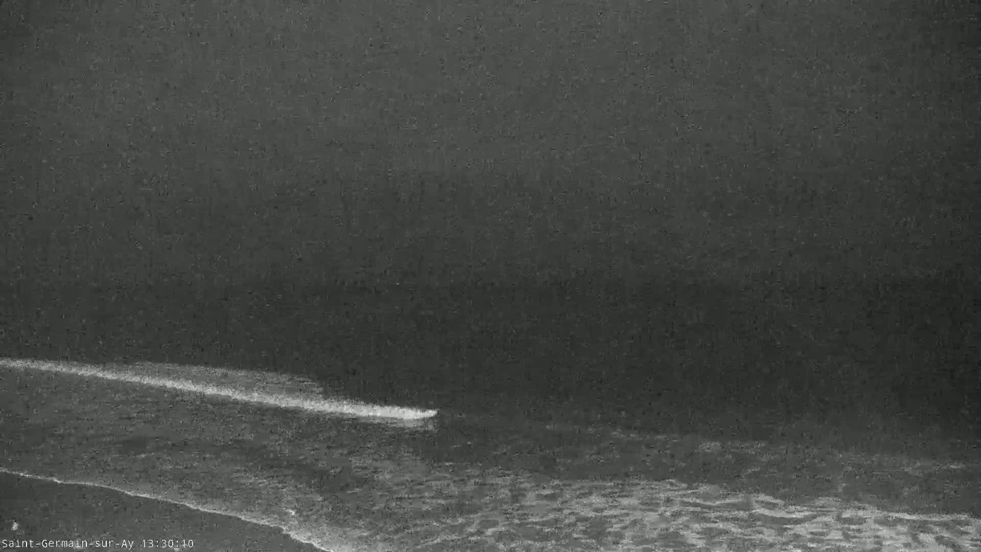 A dark, overcast sky looms over a shoreline where small waves gently lap at the beach.
