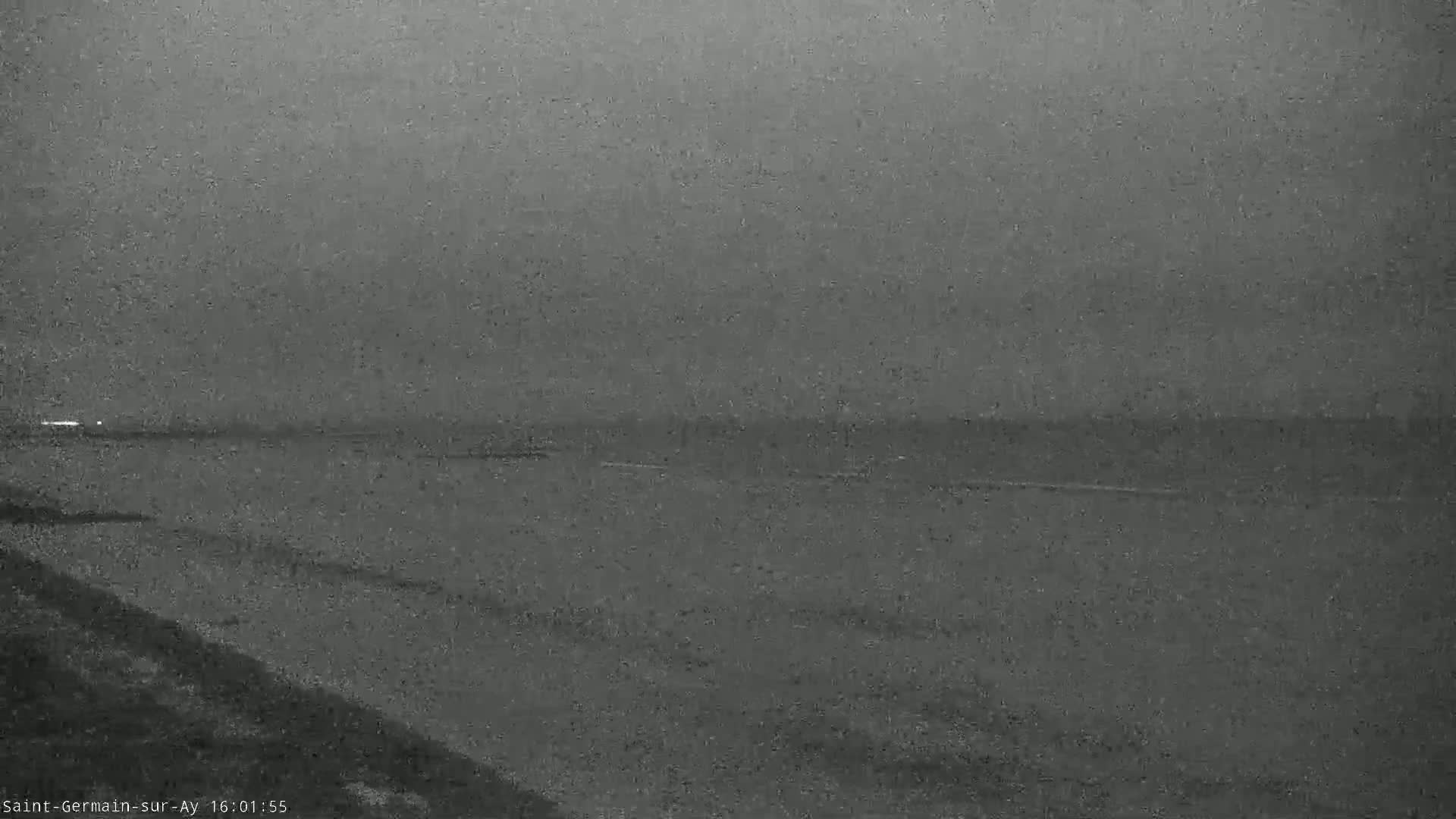 A dark, overcast sky hangs over a calm body of water, with a sloping shoreline in the foreground.