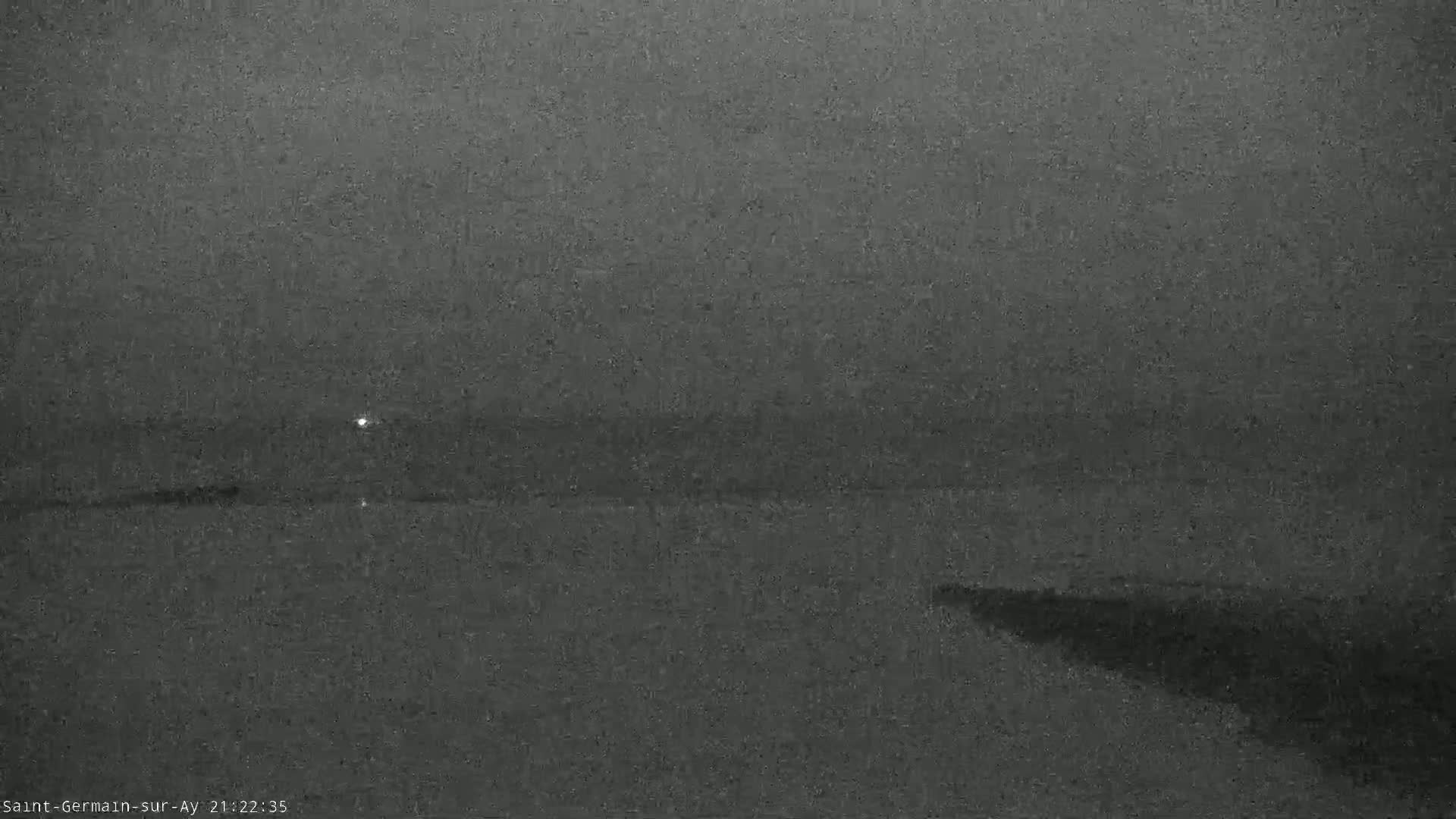 A dark, grainy image shows a body of water under a dim, overcast sky at night.