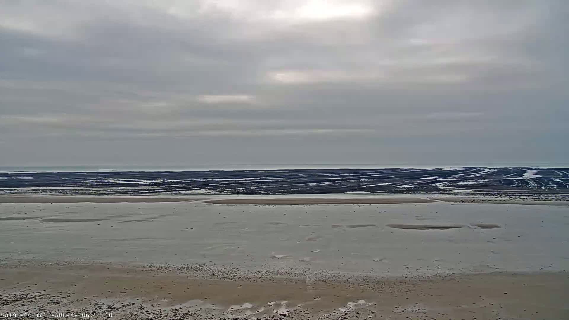 A wide, flat beach stretches to a dark, seemingly frozen, tidal flat under a cloudy sky.