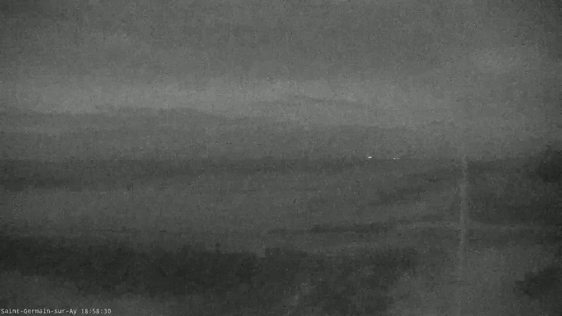 A low-light outdoor image shows a dark, hazy landscape with indistinct hills or mountains in the distance under an overcast sky.