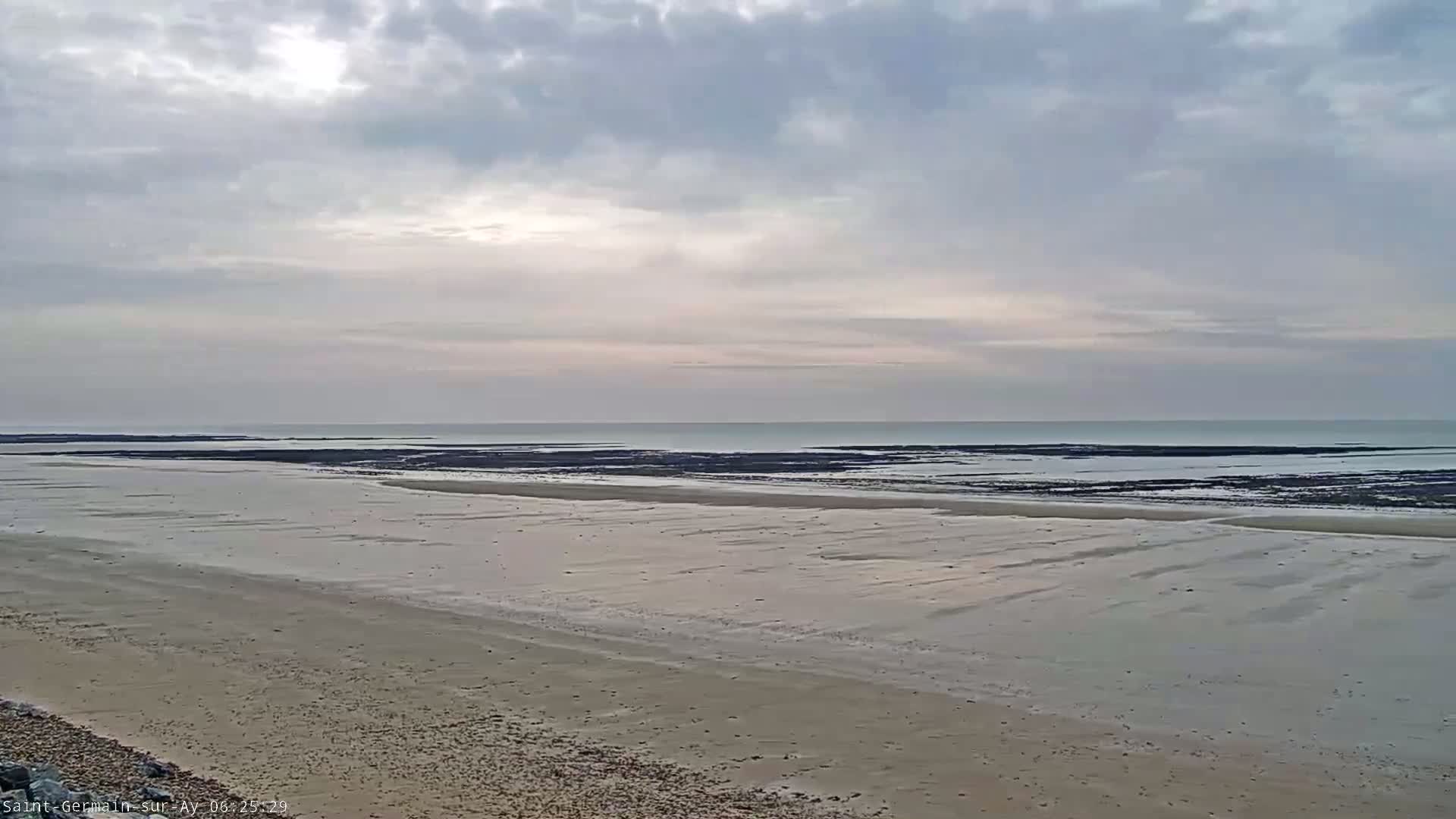 A wide sandy beach stretches towards a calm sea under a cloudy sky.