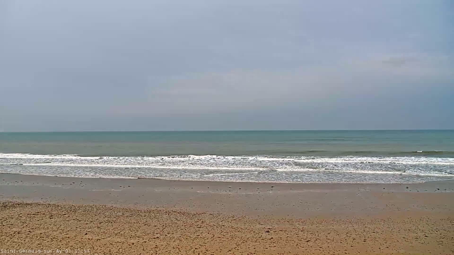 A sandy beach with gentle waves rolling onto the shore under a cloudy sky.