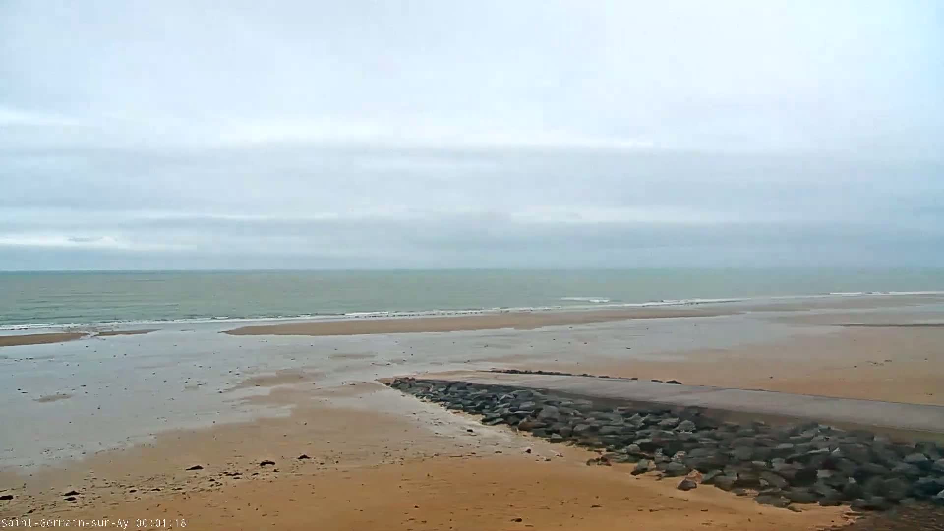 A wide sandy beach stretches to a calm, grey-toned ocean under an overcast sky.