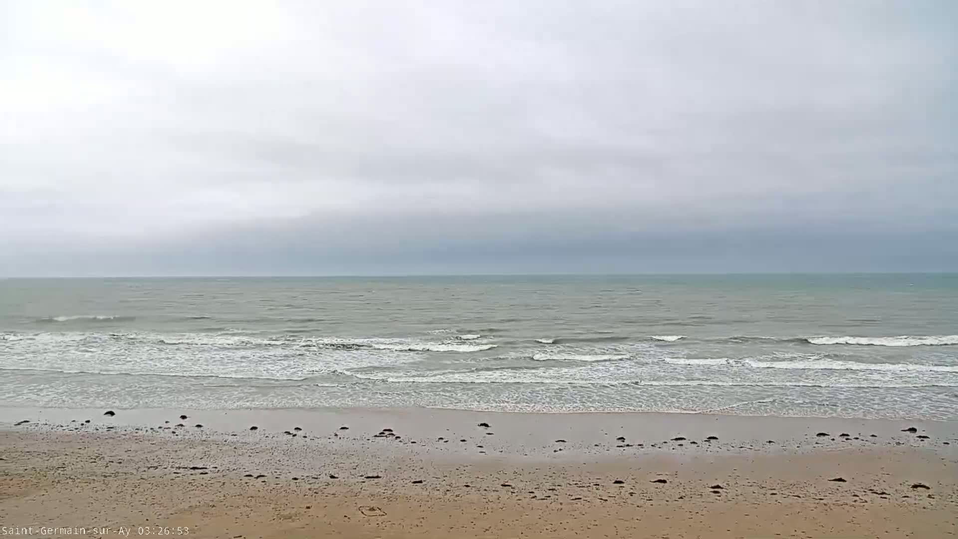 A sandy beach with small waves rolling onto the shore under an overcast sky.