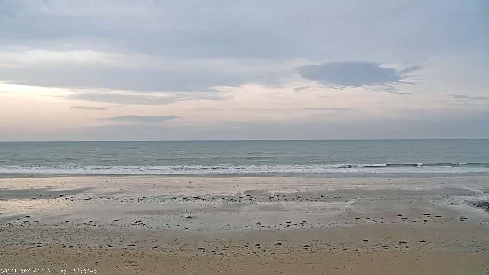 A sandy beach stretches to a calm, gray-blue ocean under a mostly cloudy sky.