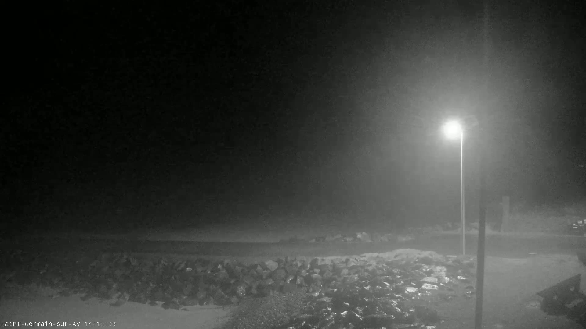 A nighttime scene shows a rocky shoreline under foggy conditions illuminated by a single lamppost.