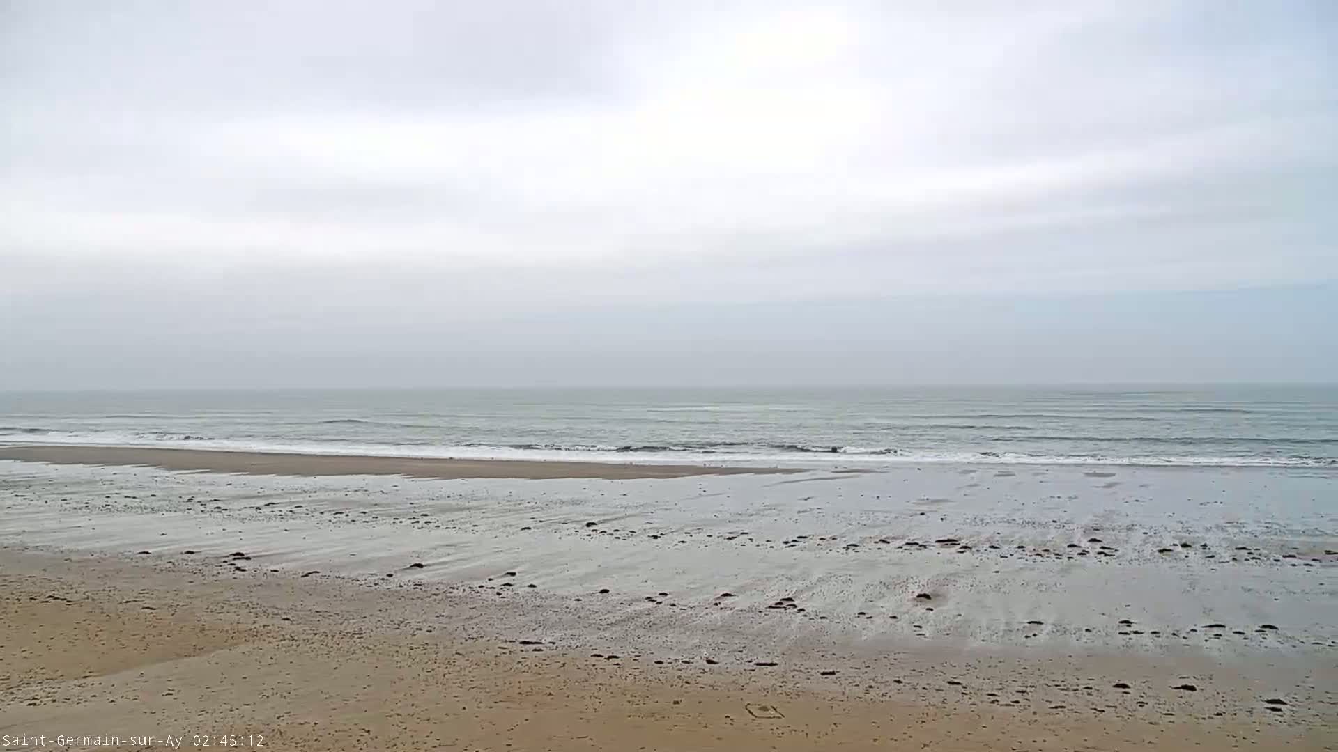 A wide, sandy beach stretches to a calm, grey ocean under an overcast sky.