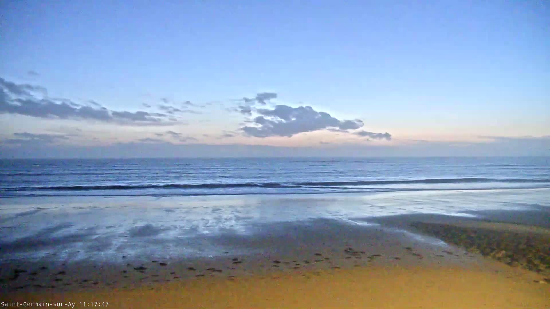 Under a mostly clear, twilight sky, gentle waves lap a sandy beach.