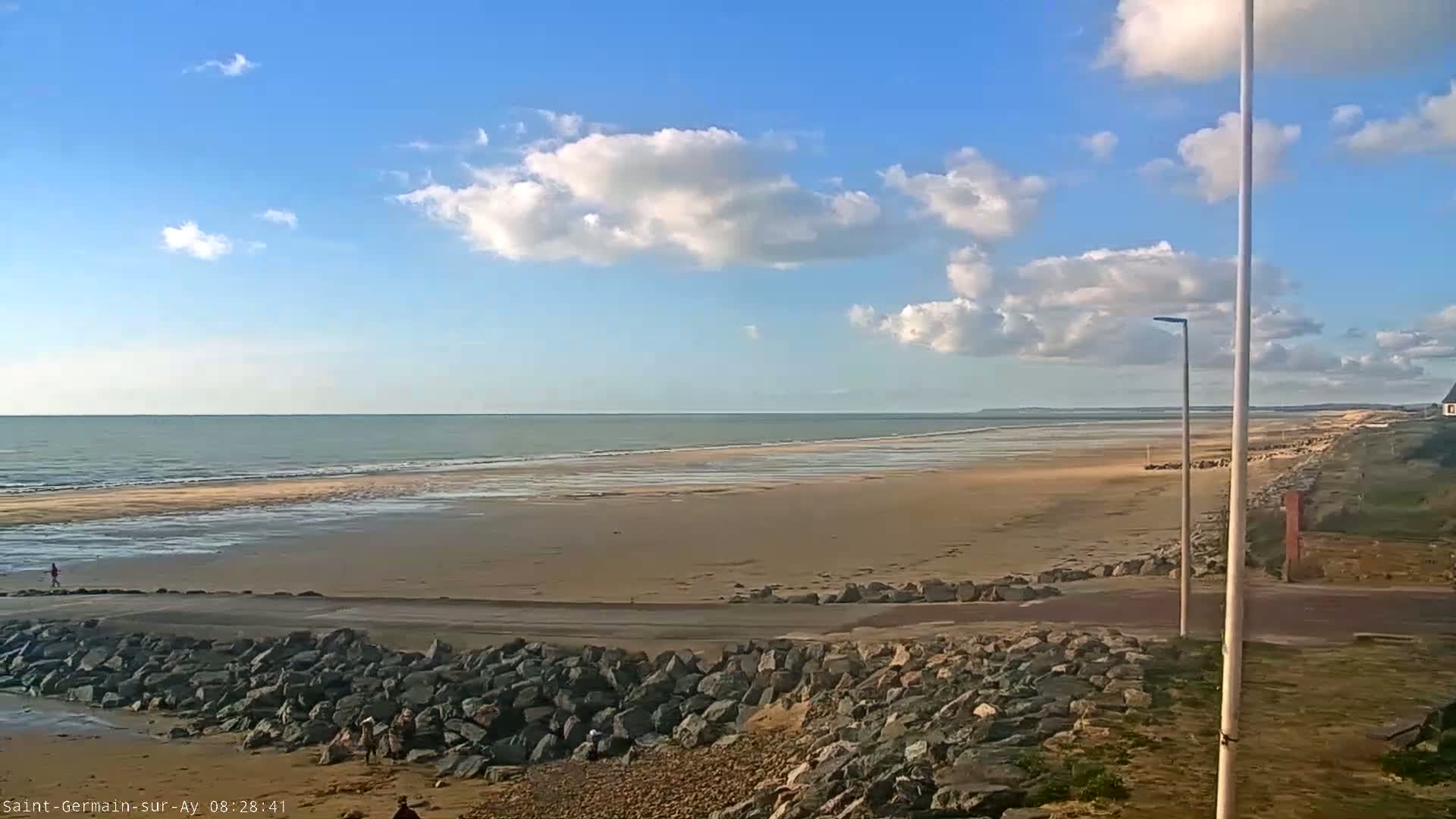 A wide sandy beach stretches to a calm ocean under a partly cloudy blue sky.