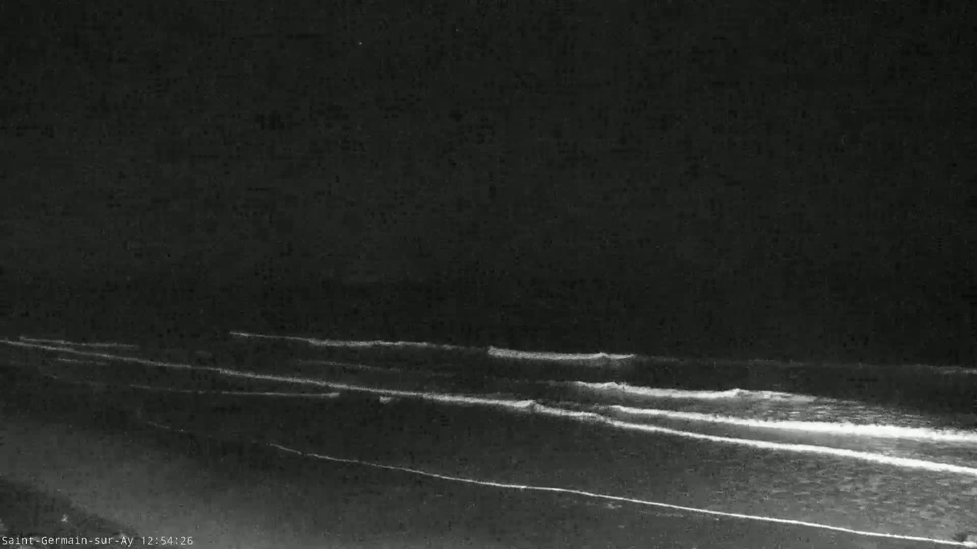 Gentle waves roll onto a dark beach under a nighttime sky.