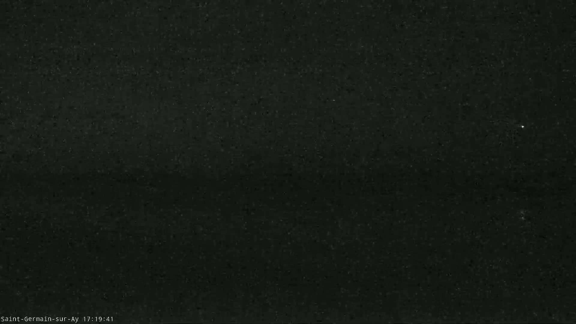 A dark, grainy image shows a mostly clear night sky with a few faint stars visible.
