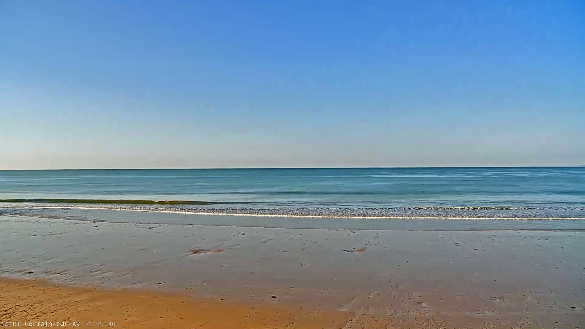A sandy beach stretches to a calm, teal ocean under a clear blue sky.