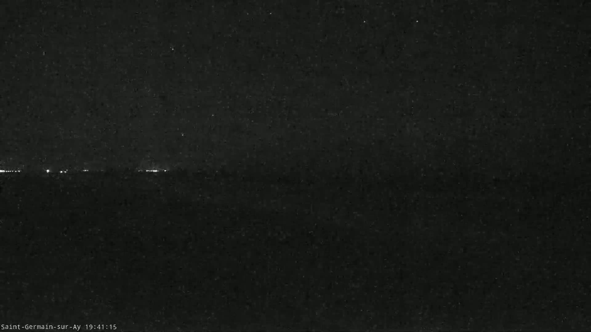 A nighttime, low-light image shows a dark horizon line with faint, distant lights.
