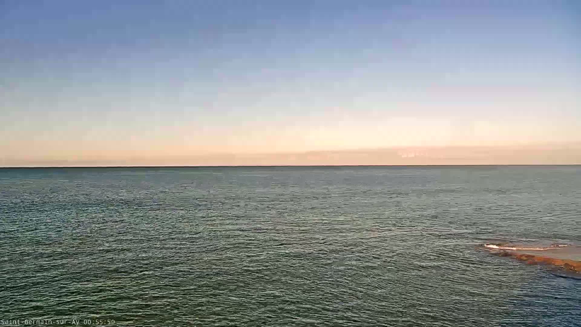 A calm, dark-green body of water stretches to a pale, pinkish-orange horizon under a clear, light-blue sky.