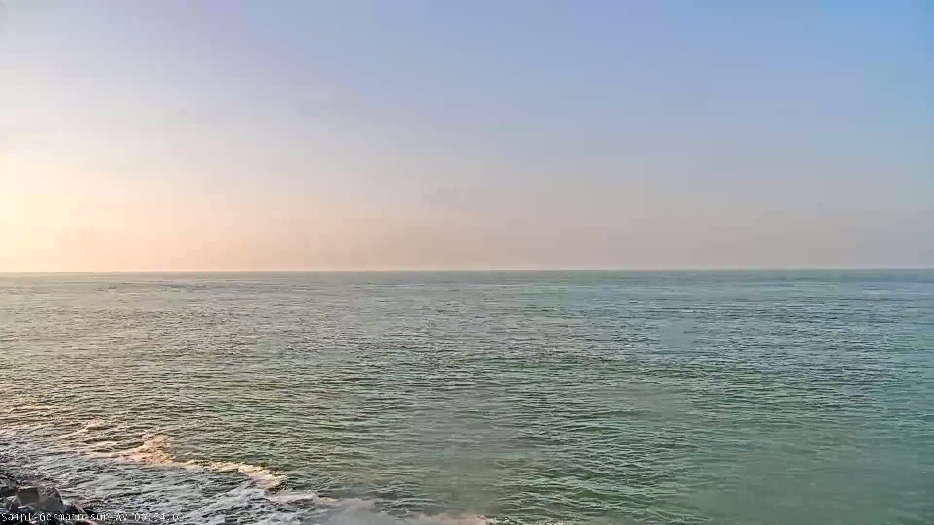 A calm, greenish-blue ocean stretches to a pale, hazy horizon under a clear, light-blue sky.