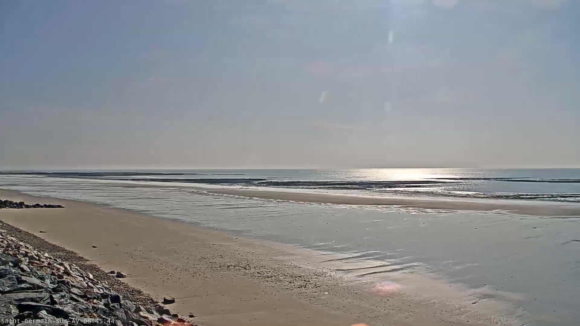 A sandy beach stretches towards a calm, sunlit ocean under a clear sky.
