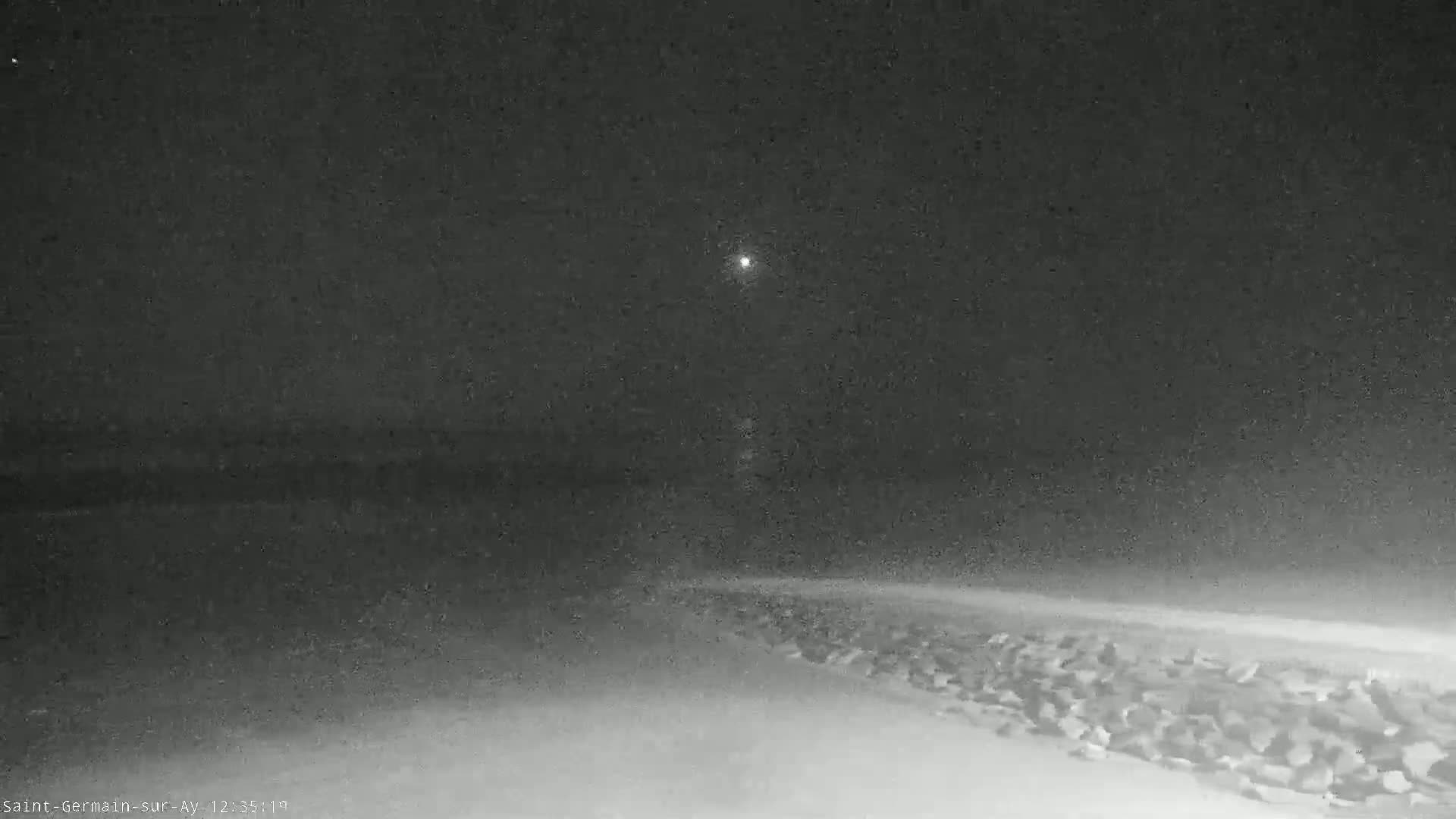 A nighttime, snow-covered shoreline with a rocky embankment is visible under a dark, cloudy sky.