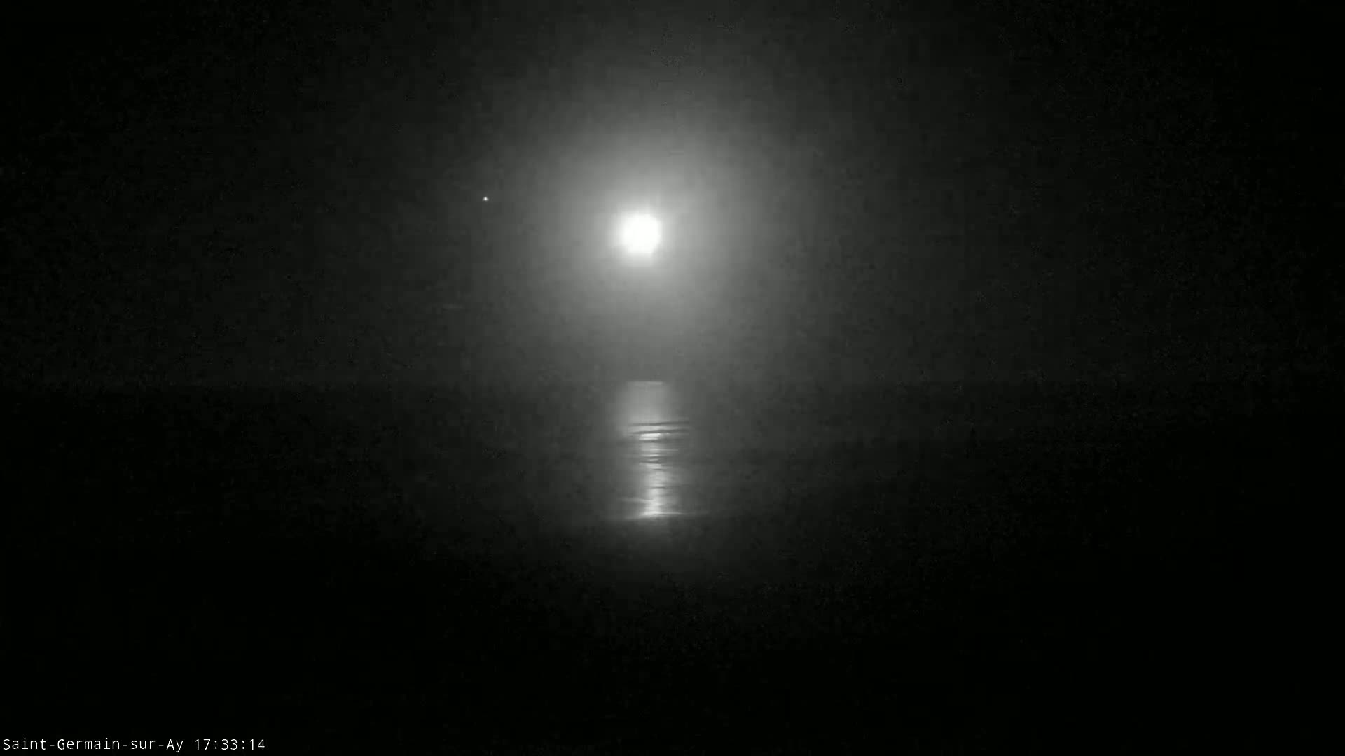 A bright moon shines over a dark body of water on a hazy night.