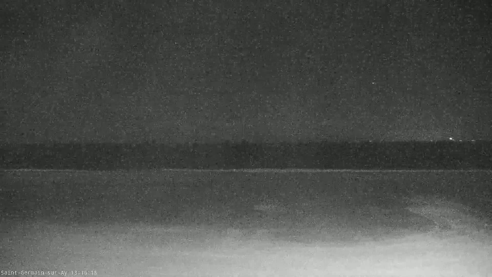 A dark, nighttime image shows a blurry, horizontal line representing a distant treeline over a lighter-toned, possibly snowy or sandy ground.