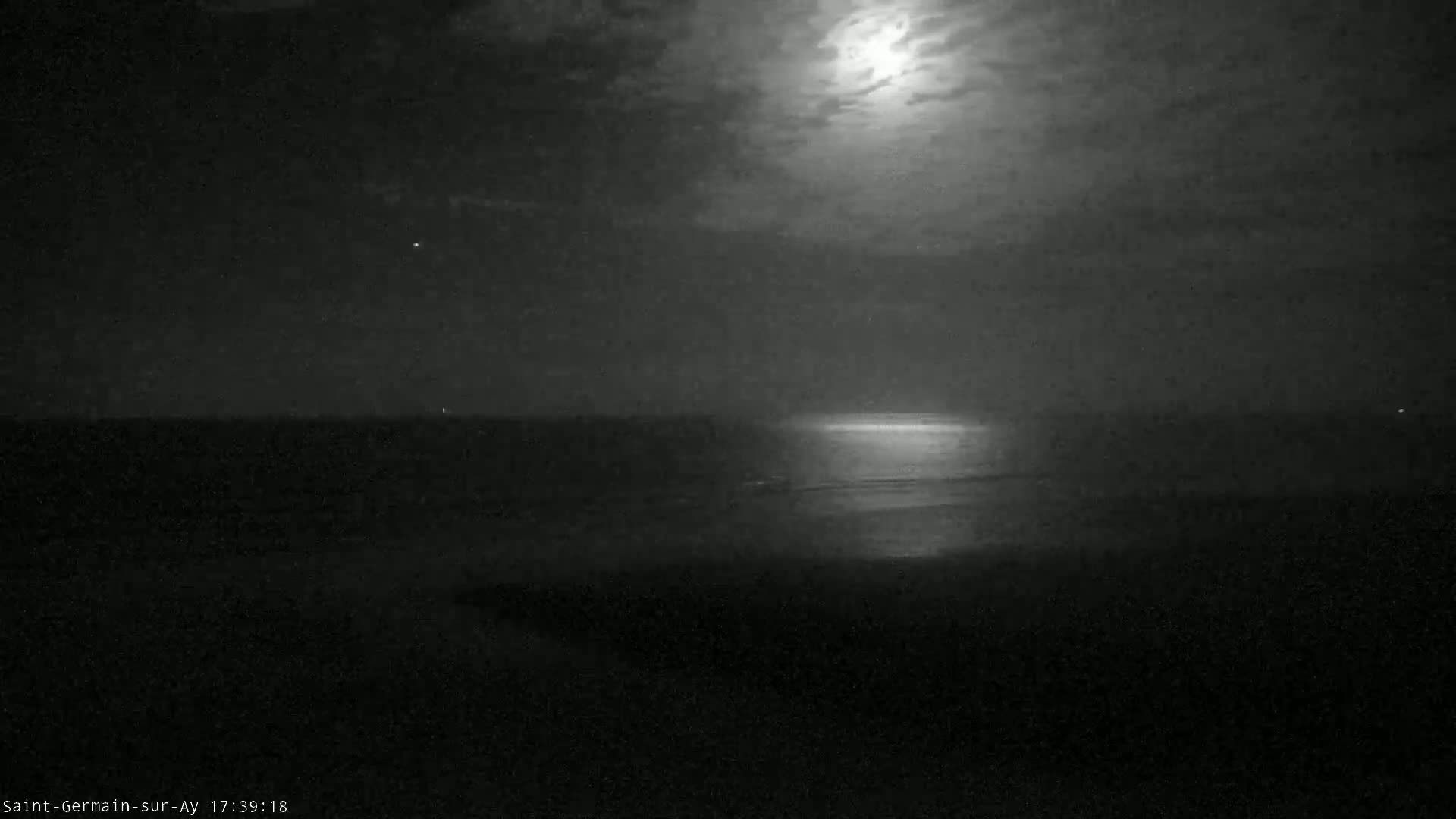 A bright moon illuminates a dark, nighttime ocean scene with a partly cloudy sky.