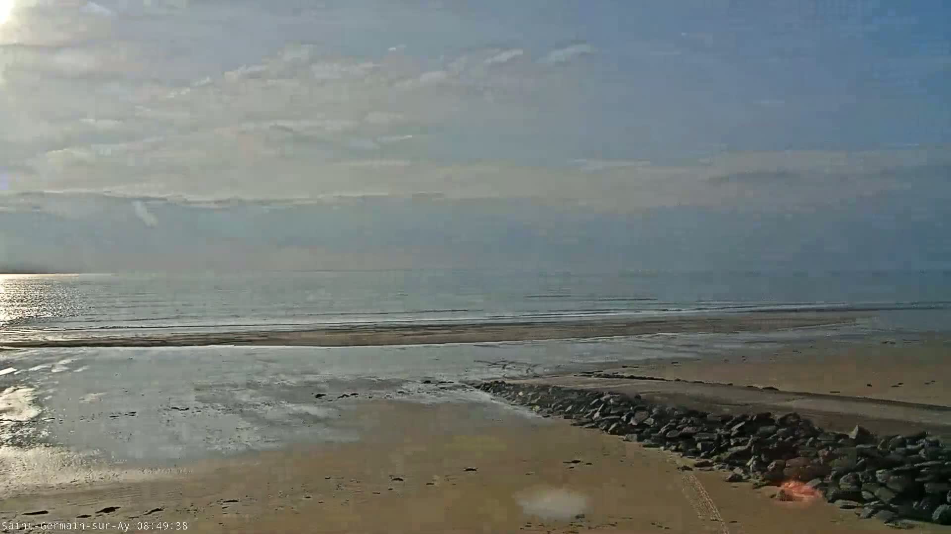 A sandy beach with a calm ocean under a partly cloudy sky.