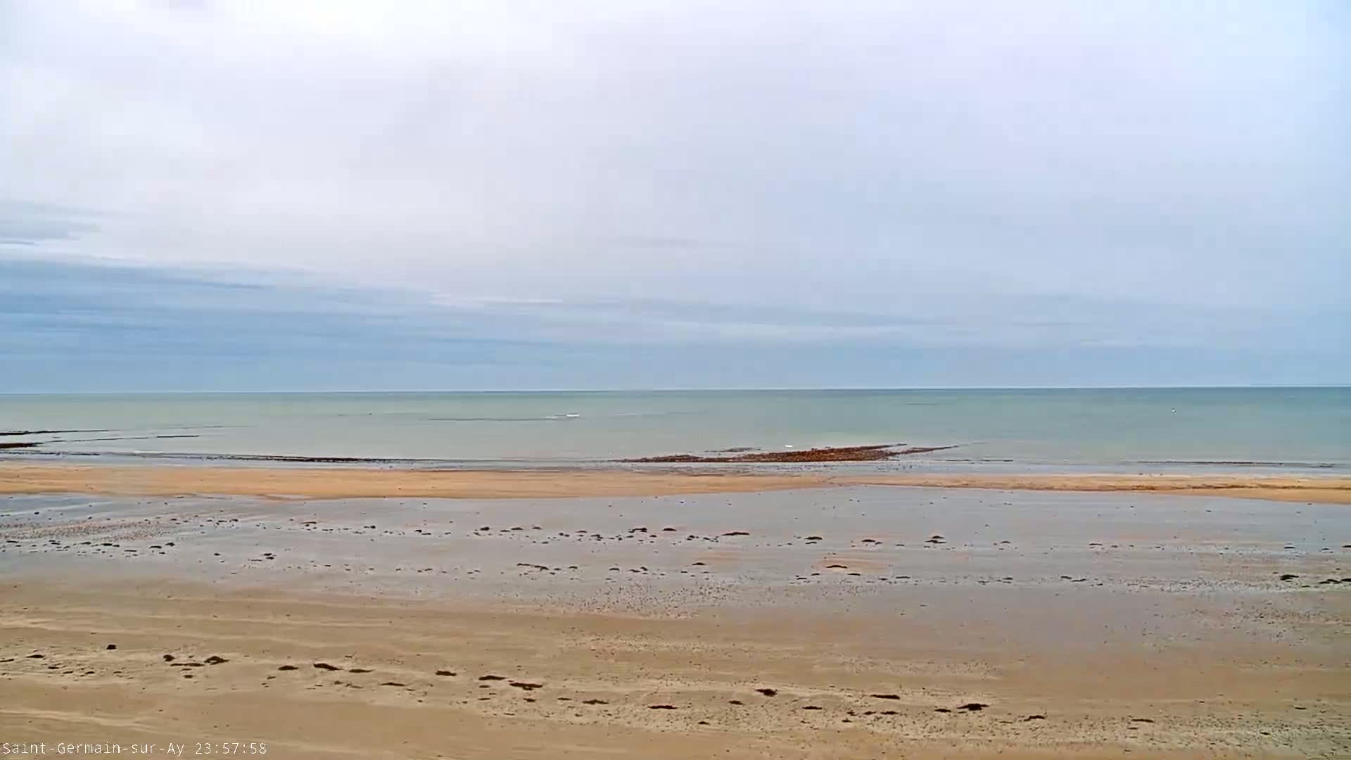 A sandy beach stretches to a calm, light-blue ocean under a mostly cloudy sky.