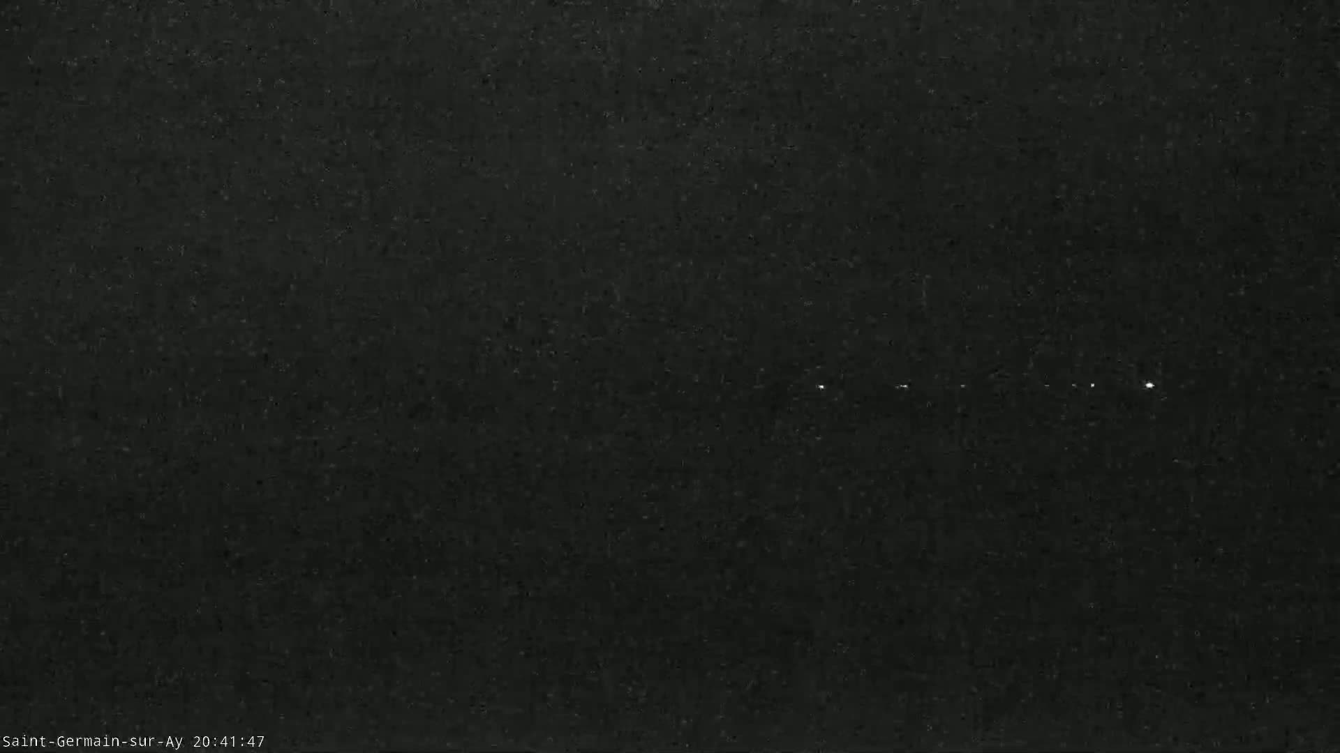 A dark, grainy image shows a few faint, bright lights in the distance under a dark night sky.