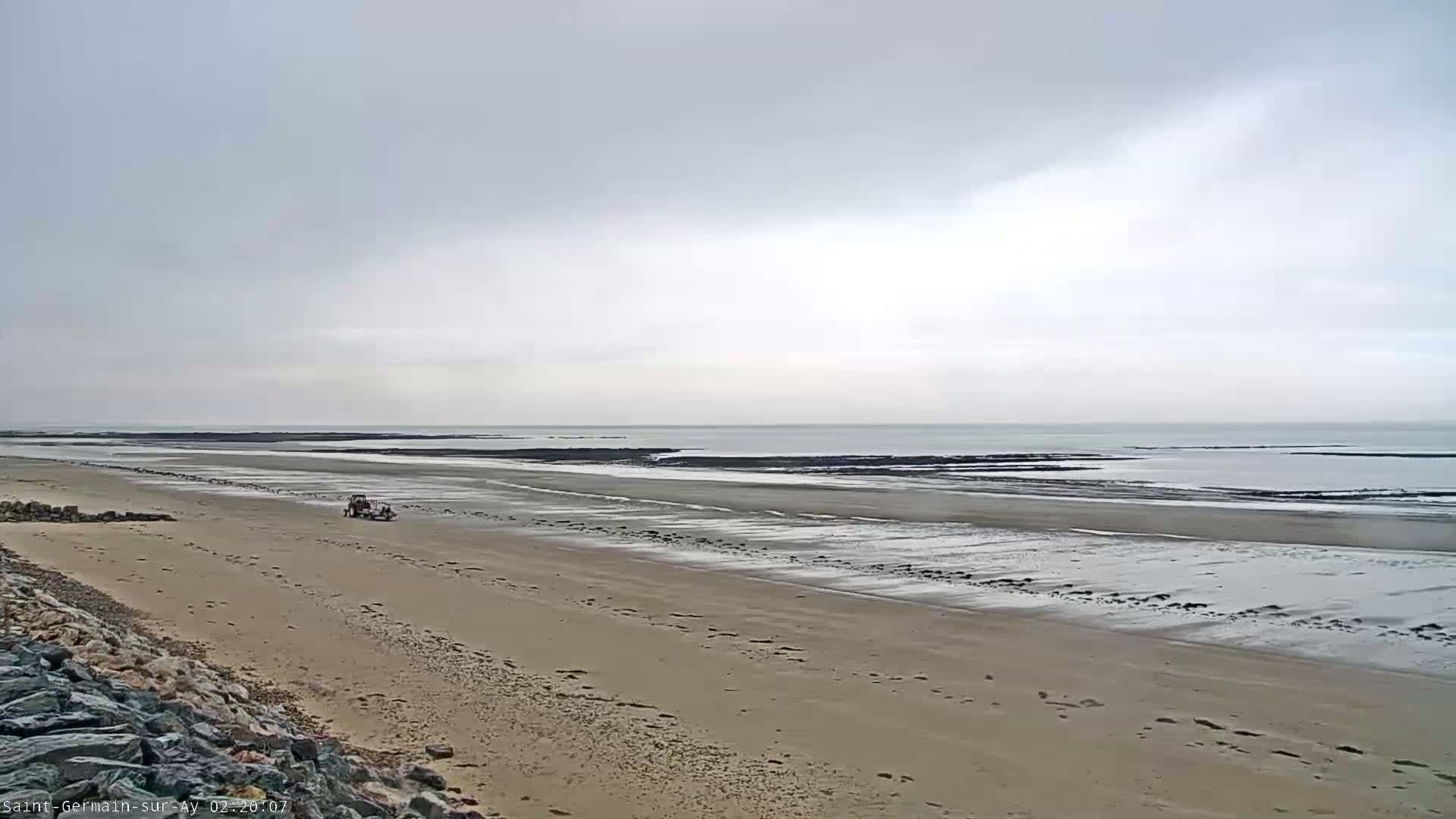 A wide sandy beach stretches toward a calm, gray sea under an overcast sky.