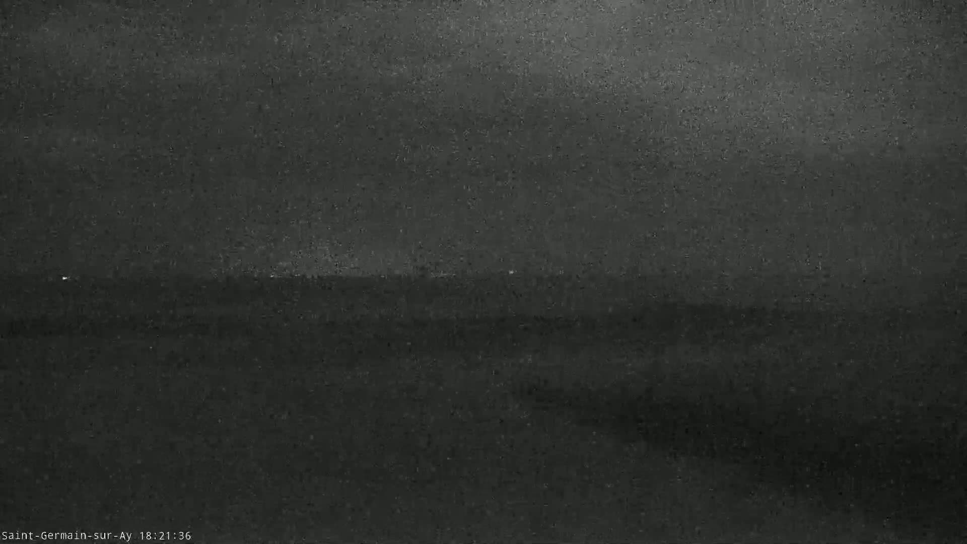 A dark, grainy image shows a dimly lit landscape under a cloudy night sky.