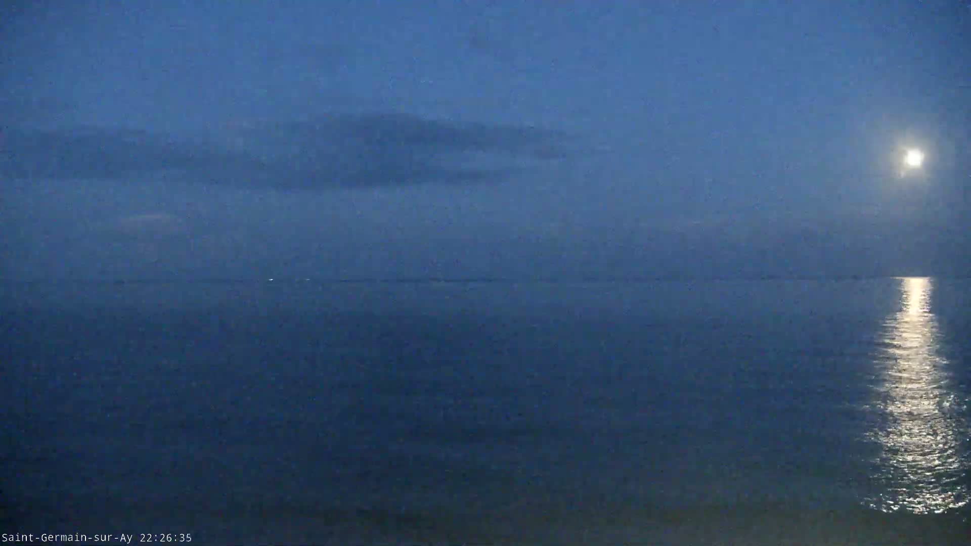A calm, dark blue sea is illuminated by moonlight under a mostly clear, twilight sky.