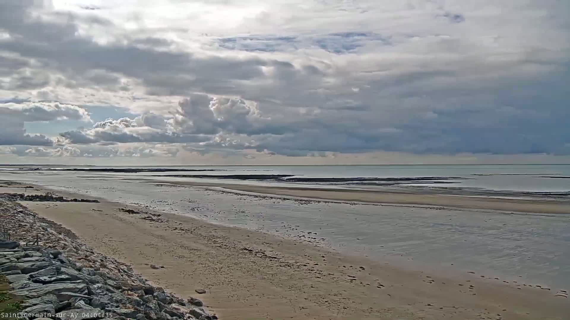 A sandy beach stretches towards a calm sea under a partly cloudy sky.