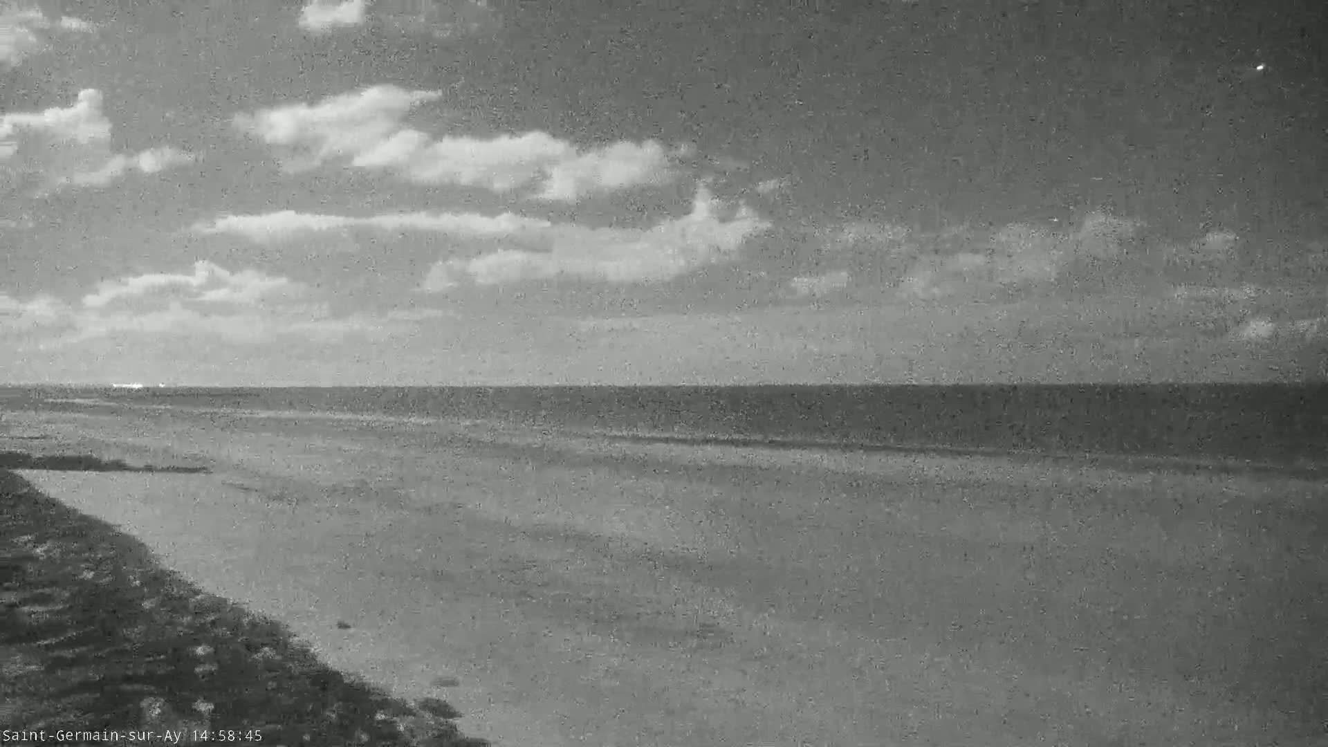 A mostly cloudy sky overlooks a calm ocean and a sandy beach at night.