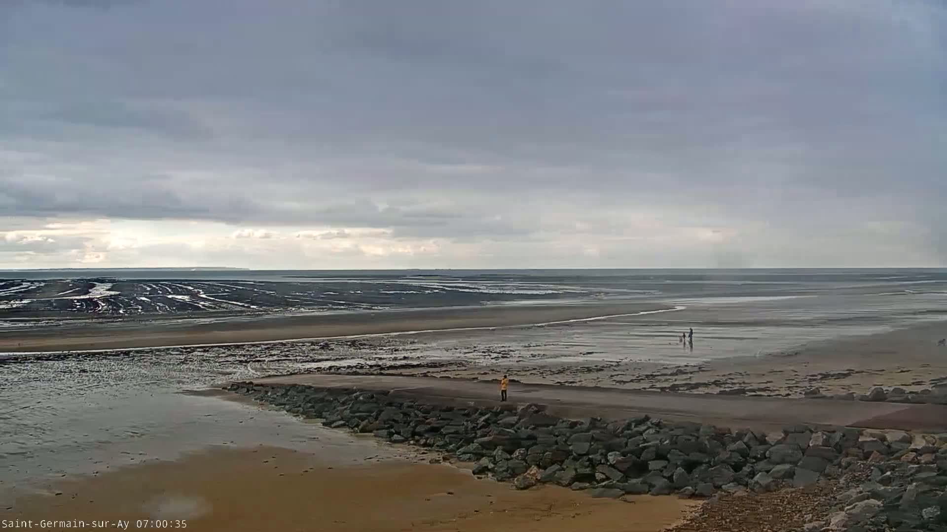 A wide expanse of muddy beach and shallow water stretches to a calm, grey sea under an overcast sky.