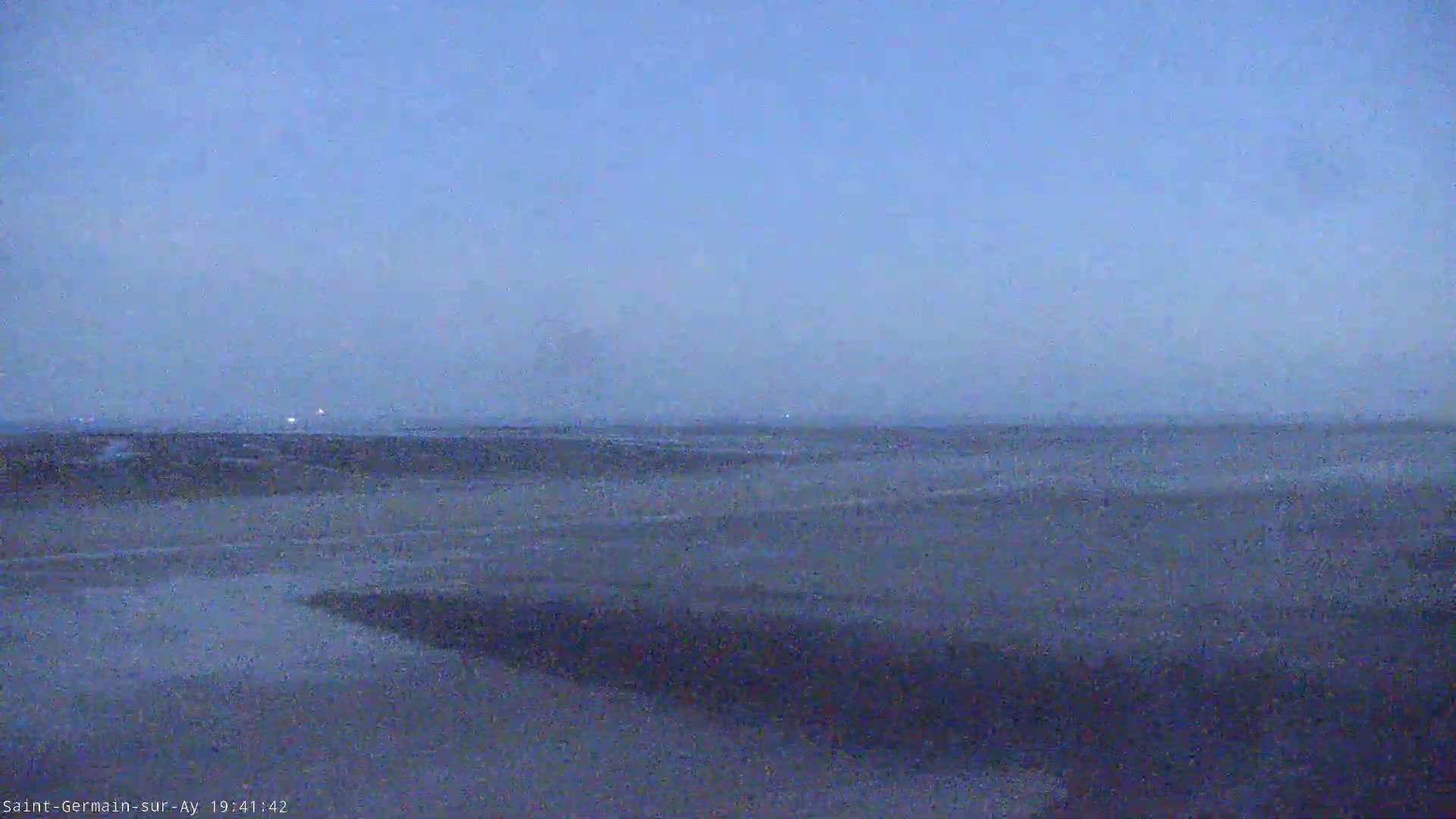 A hazy, dark blue sky overlooks a flat, dark land under twilight conditions.