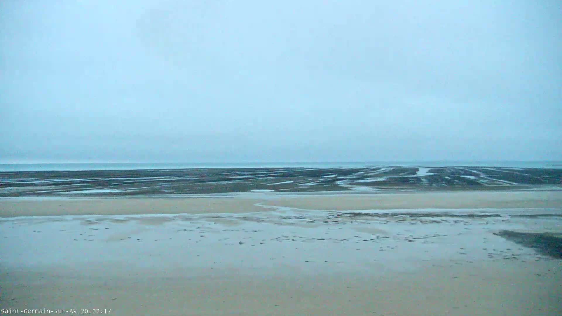 A wet, sandy beach stretches to a calm, gray ocean under an overcast sky.