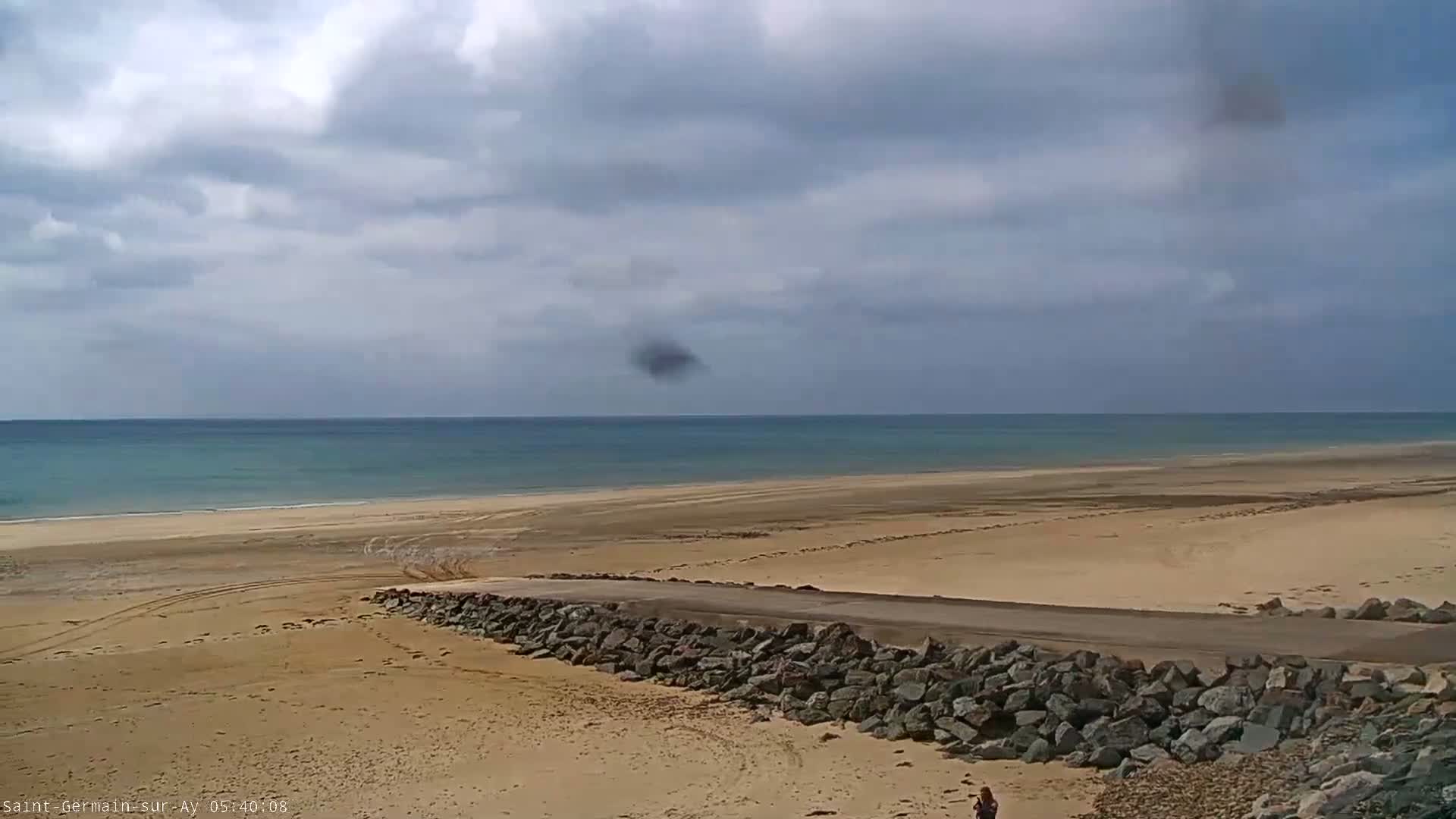 A sandy beach stretches to a calm, light-blue ocean under a mostly cloudy sky.