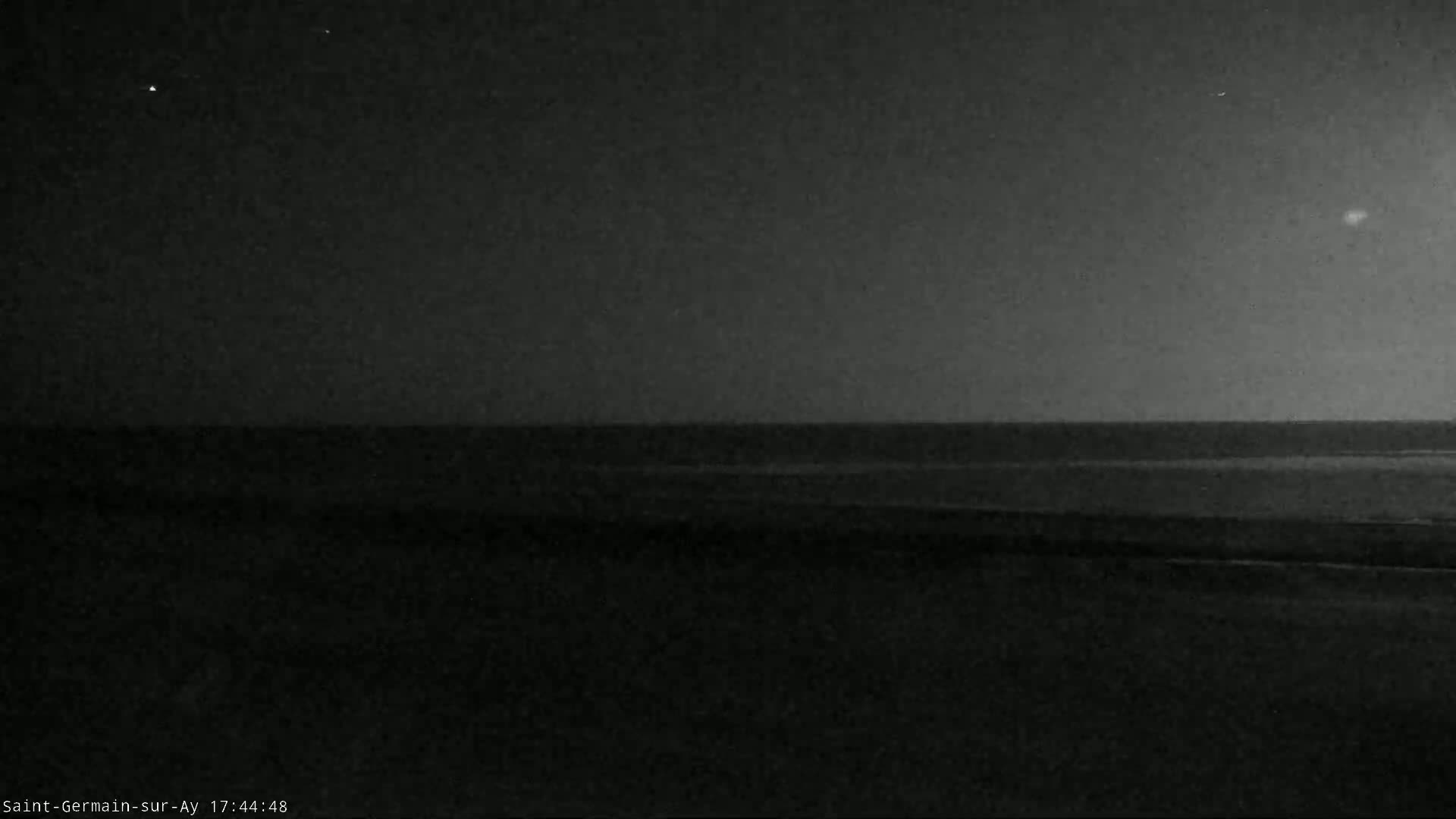 A dark, nighttime beach scene shows a calm body of water under a clear, starry sky.