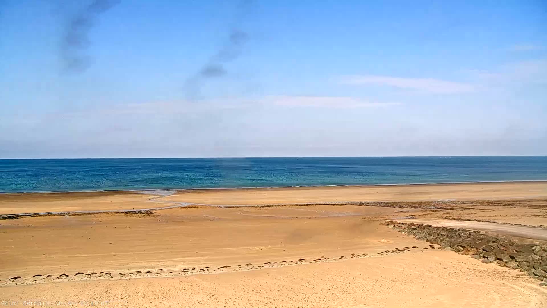 A sandy beach stretches to a calm, blue ocean under a mostly clear sky.