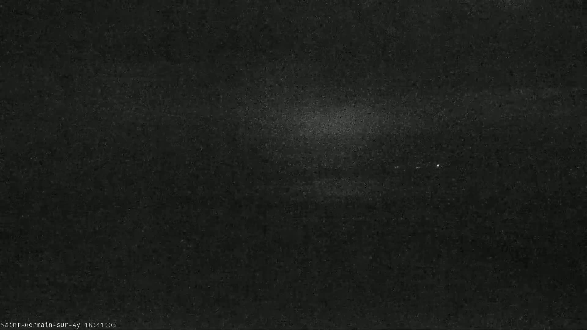 A dark, grainy image shows a dimly lit, possibly nighttime scene with a few faint lights in the distance.