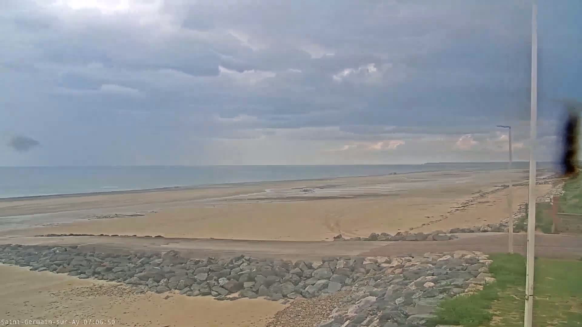 A wide sandy beach stretches to a calm ocean under a cloudy sky.