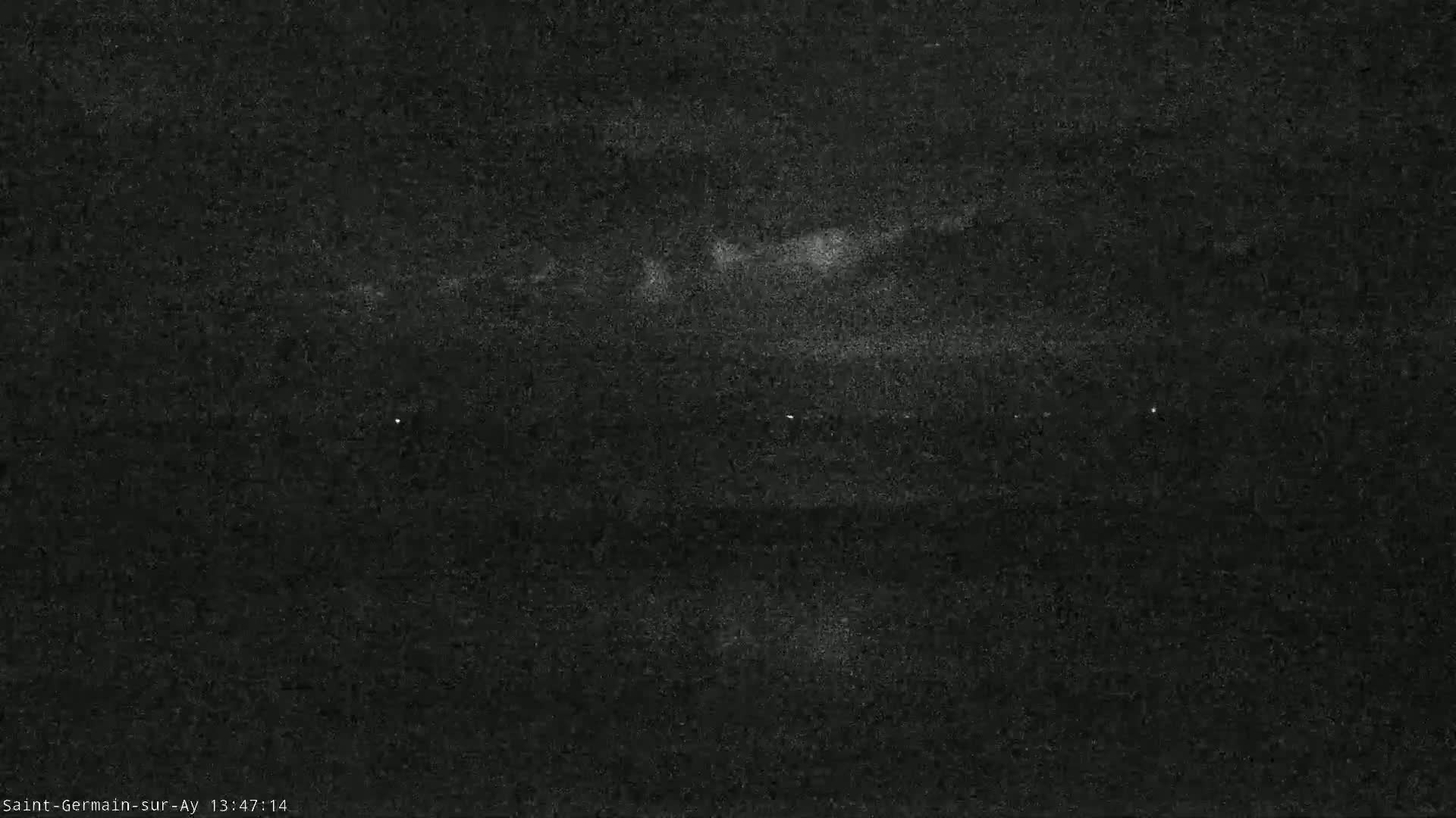 A nighttime, low-light image shows a dark, possibly overcast sky above a dark body of water with faint, distant lights visible on the horizon.