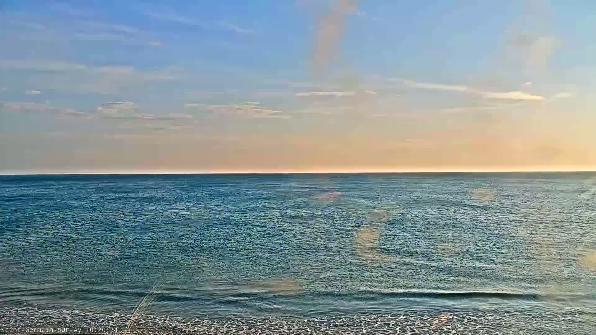 A calm ocean meets a pale, sunset sky under a mostly clear sky.